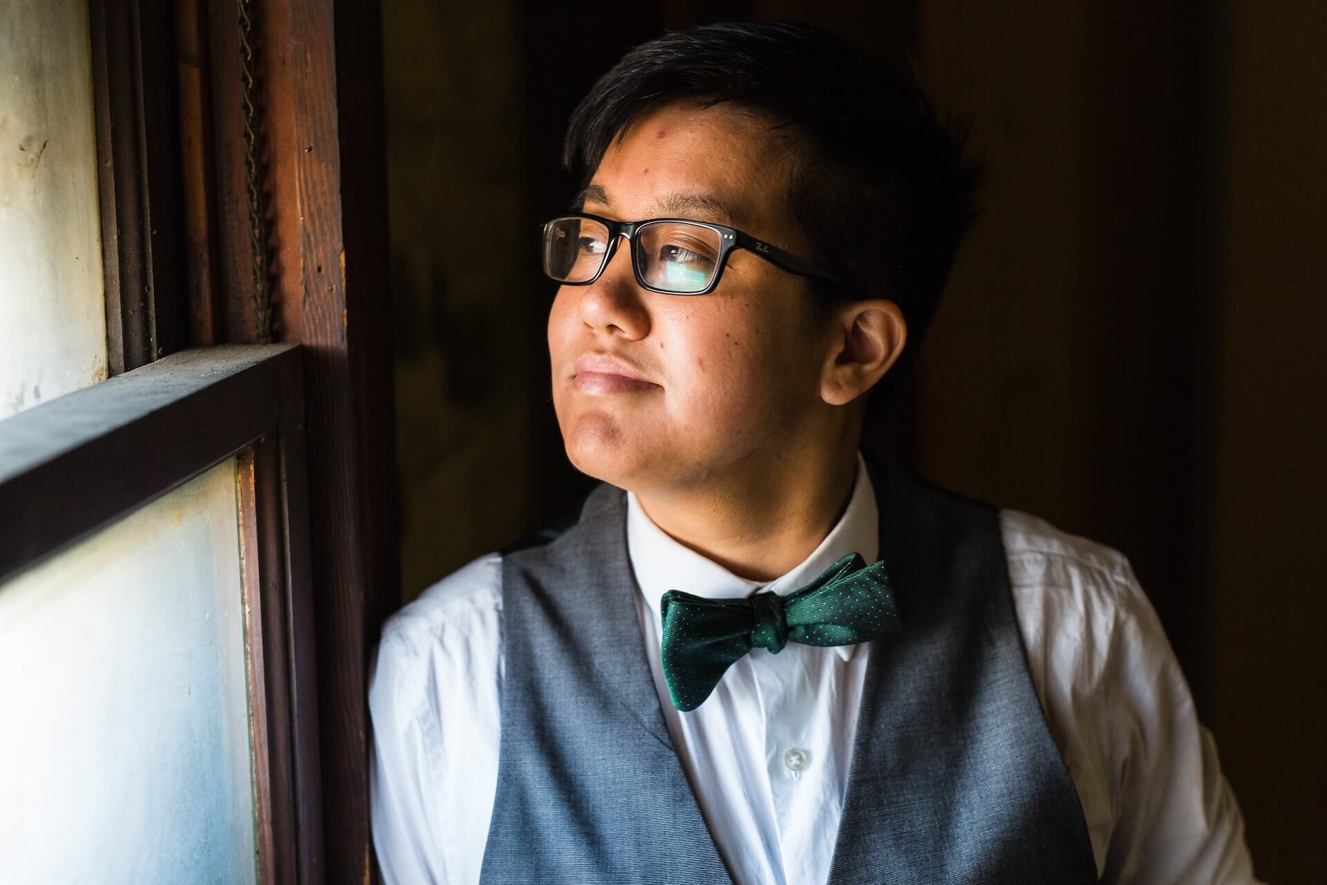Young person in vest and bow tie looking thoughtfully out a window representing transgender fertility preservation options at FCLV