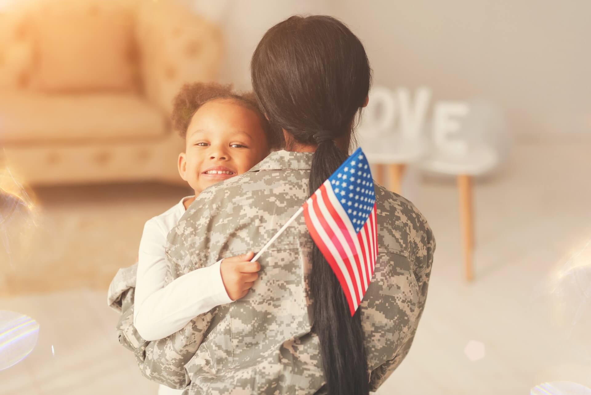 Female military service member in uniform holding child with American flag representing fertility care and IVF coverage for military families