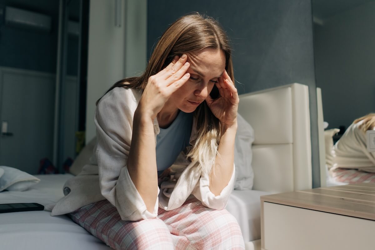 Woman sitting on a bed holding her temples, appearing stressed and overwhelmed